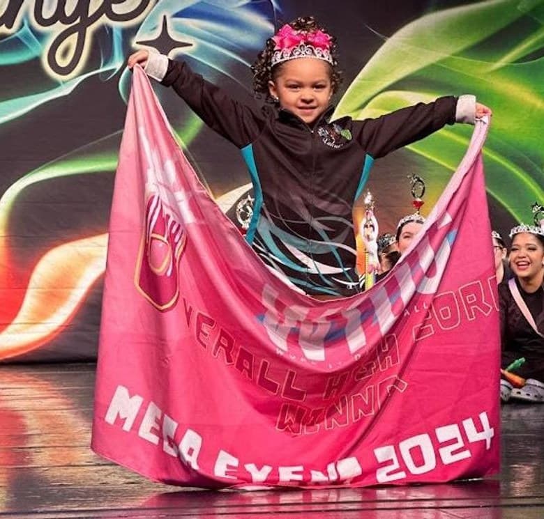 Young dancer in a crown holding the pink Mega Event Overall High Score banner