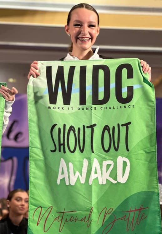Dancer smiling behind a green WIDC Shout Out Award flag