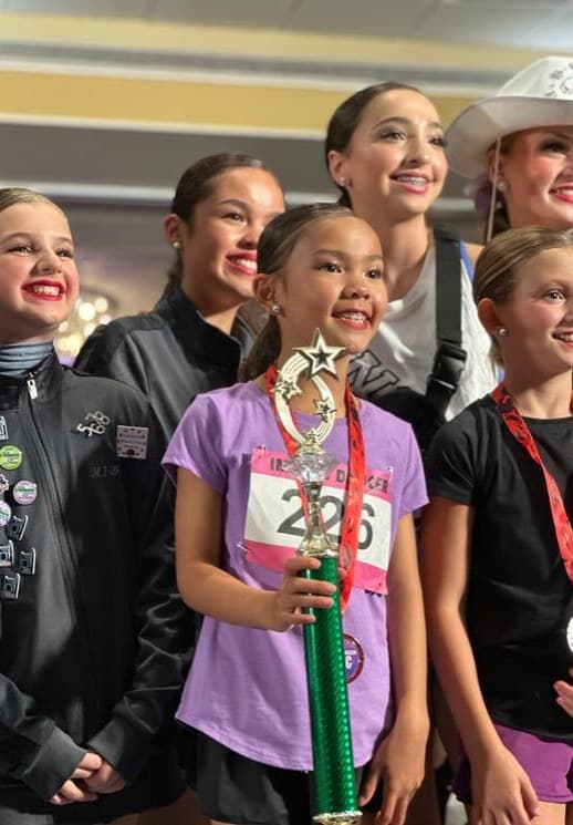 Smiling young dancer holding a star trophy with her teammates