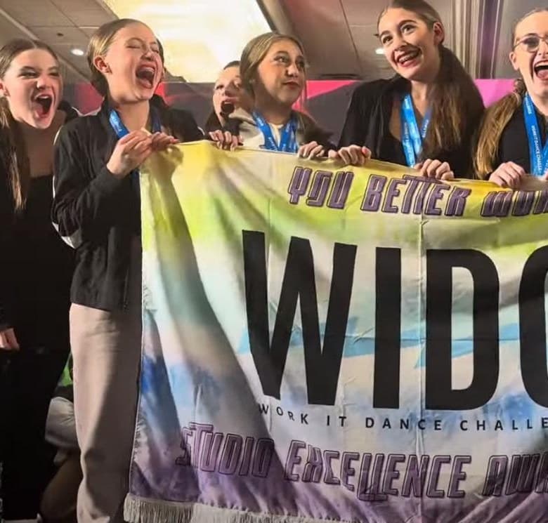 Dancers cheering behind the WIDC Studio Excellence banner