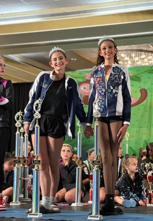 Two title winners in crowns holding hands on stage