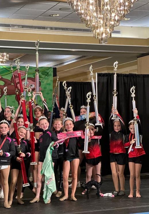 Team raising their trophies on stage under a ballroom chandelier